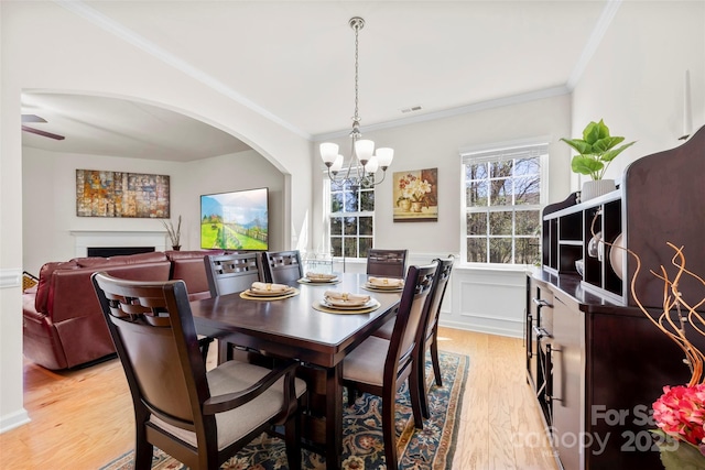dining space featuring a wainscoted wall, an inviting chandelier, light wood-style flooring, a fireplace, and ornamental molding