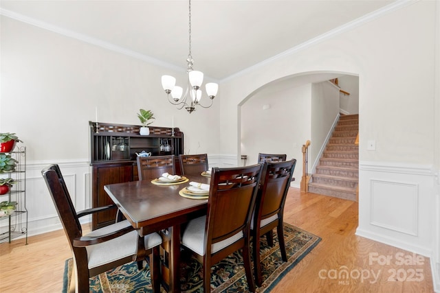 dining area featuring arched walkways, stairs, light wood-style floors, wainscoting, and crown molding