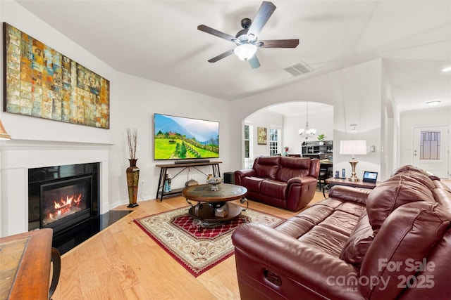 living room with visible vents, ceiling fan with notable chandelier, wood finished floors, arched walkways, and a glass covered fireplace