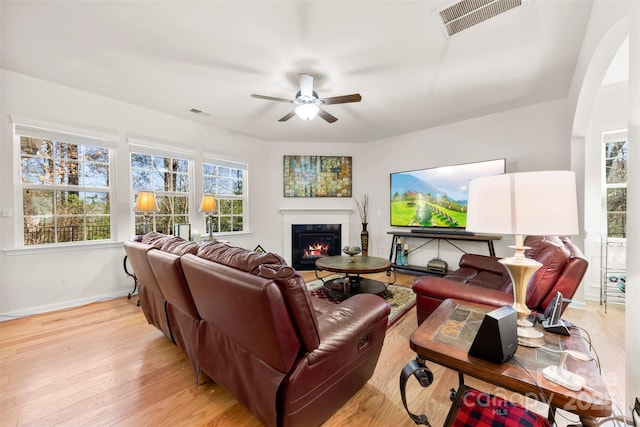 living room with visible vents, light wood-style flooring, a ceiling fan, a glass covered fireplace, and baseboards