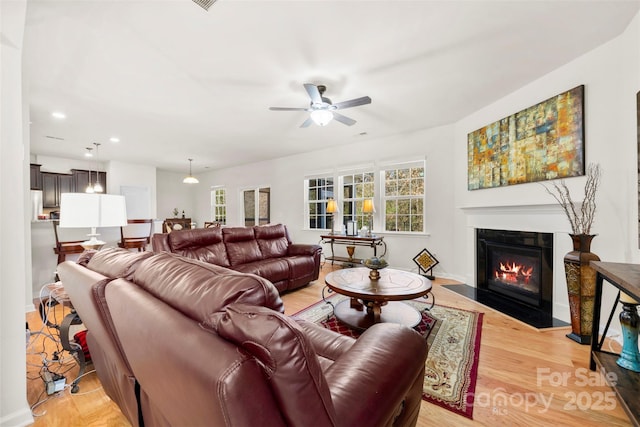 living room featuring baseboards, ceiling fan, a fireplace with flush hearth, recessed lighting, and light wood-style floors