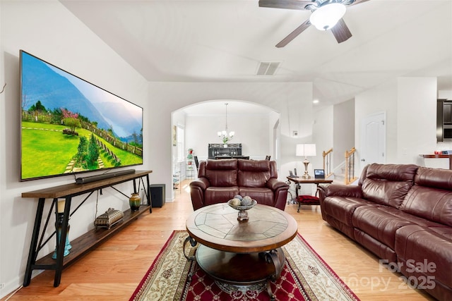 living area featuring visible vents, baseboards, light wood-style flooring, arched walkways, and ceiling fan with notable chandelier
