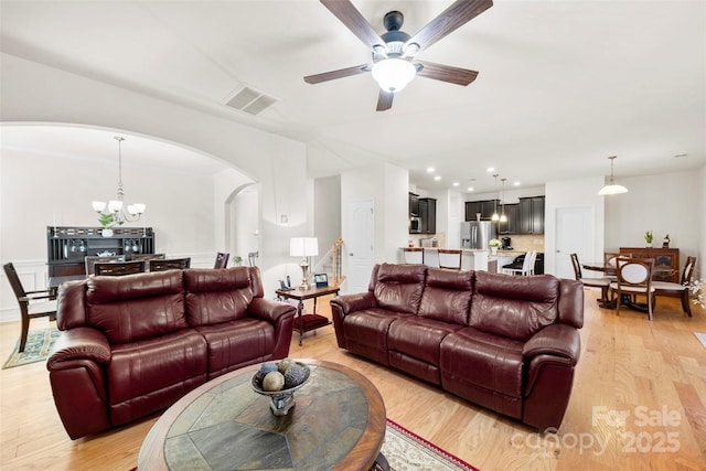 living room featuring arched walkways, visible vents, light wood-style flooring, and ceiling fan with notable chandelier