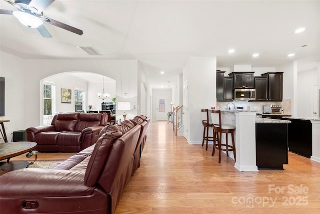 living room with visible vents, light wood finished floors, a toaster, arched walkways, and ceiling fan with notable chandelier