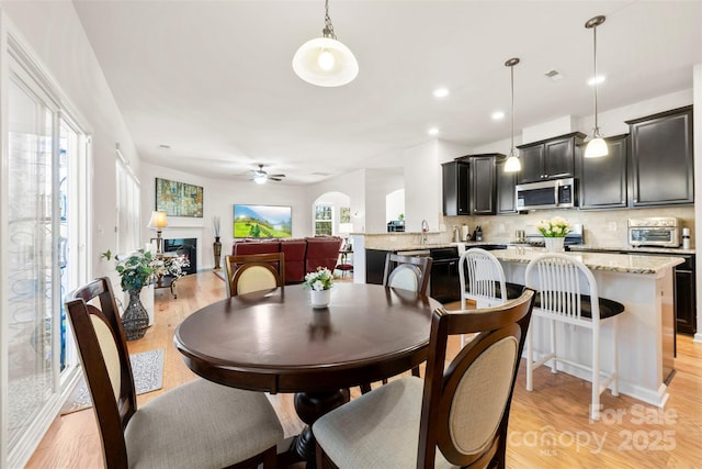 dining space featuring a ceiling fan, a toaster, recessed lighting, a fireplace, and light wood-type flooring