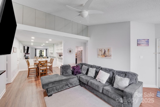 living room featuring baseboards, light wood-type flooring, recessed lighting, a textured ceiling, and a ceiling fan
