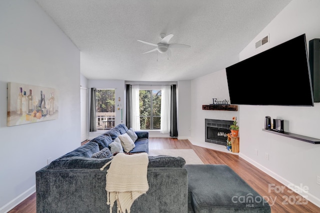 living area with visible vents, a fireplace with flush hearth, wood finished floors, and a ceiling fan