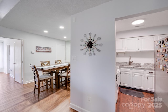 kitchen featuring light stone countertops, light wood finished floors, a sink, stainless steel refrigerator, and white cabinetry