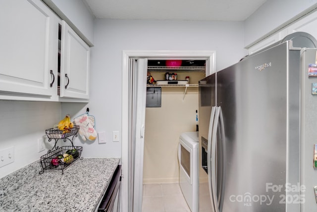 kitchen featuring light stone counters, washing machine and dryer, white cabinetry, light tile patterned flooring, and stainless steel fridge with ice dispenser