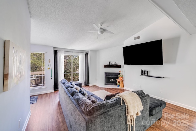 living area with visible vents, a textured ceiling, wood finished floors, a fireplace, and ceiling fan