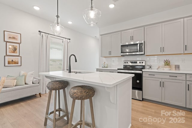 kitchen with light wood-type flooring, gray cabinetry, a sink, light stone counters, and appliances with stainless steel finishes