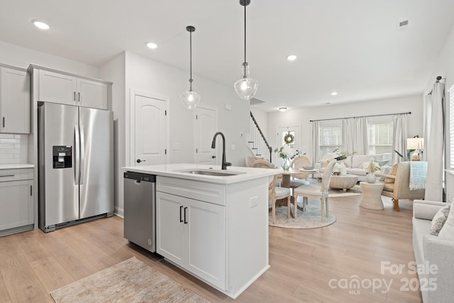 kitchen with a sink, stainless steel appliances, light countertops, open floor plan, and light wood-type flooring