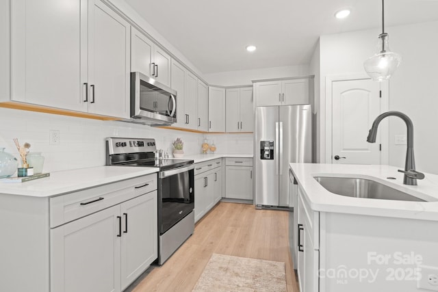 kitchen featuring light wood finished floors, a sink, decorative light fixtures, appliances with stainless steel finishes, and light countertops