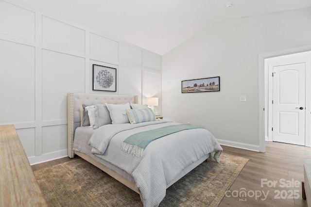 bedroom featuring vaulted ceiling, a decorative wall, wood finished floors, and baseboards