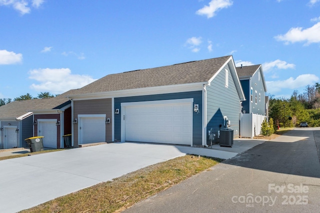 view of home's exterior featuring cooling unit, an attached garage, concrete driveway, and roof with shingles