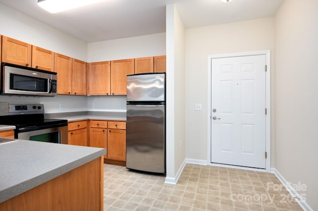 kitchen featuring stainless steel appliances, baseboards, brown cabinets, and light countertops