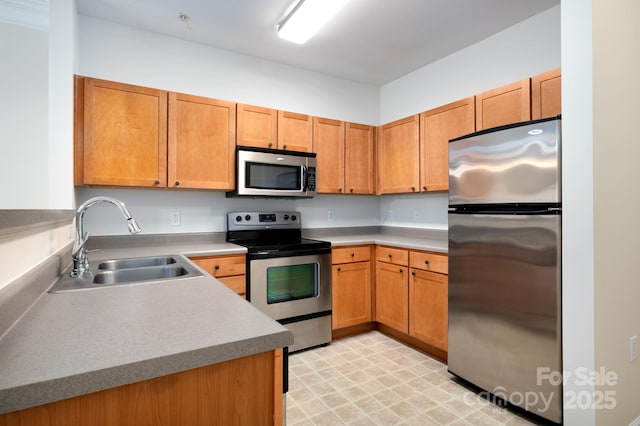 kitchen with brown cabinets, a sink, appliances with stainless steel finishes, light countertops, and light floors