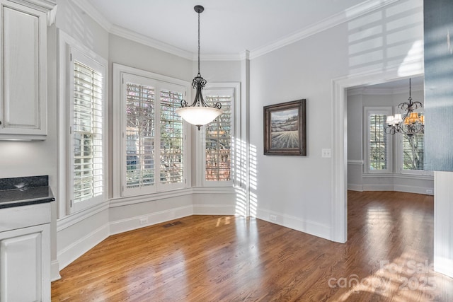 unfurnished dining area featuring a chandelier, visible vents, light wood-style flooring, and crown molding
