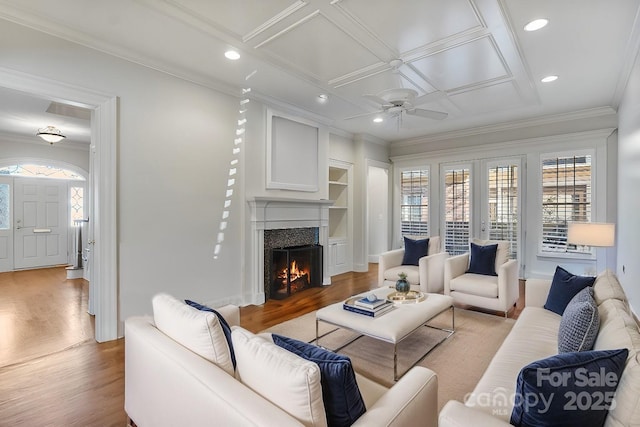 living area with coffered ceiling, a warm lit fireplace, light wood-type flooring, and ornamental molding