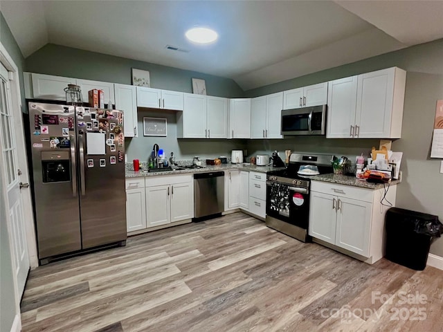 kitchen with light wood finished floors, white cabinetry, stainless steel appliances, and vaulted ceiling