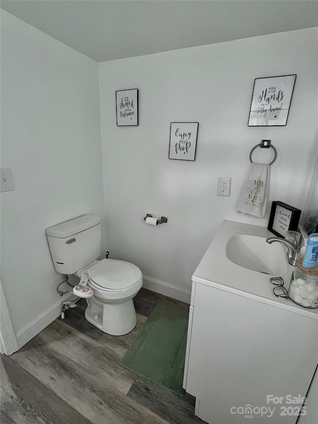 bathroom featuring baseboards, toilet, wood finished floors, and vanity