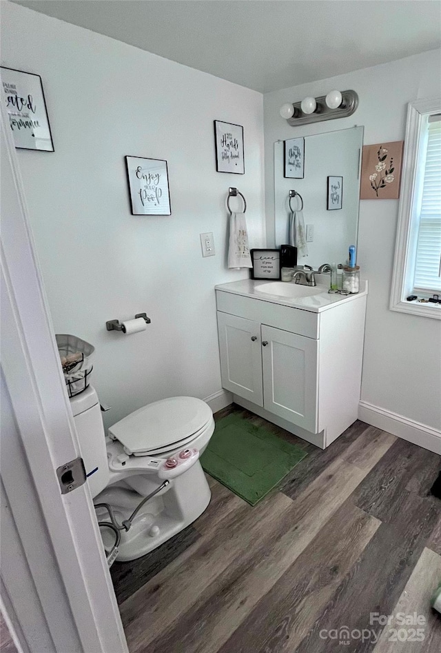 half bathroom featuring vanity, toilet, wood finished floors, and baseboards