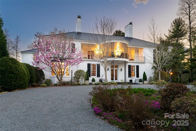 view of front of property featuring metal roof, a balcony, a chimney, and driveway