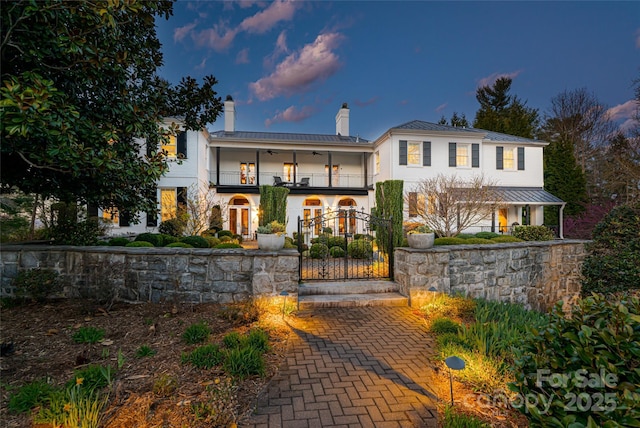 view of front of property with a balcony, a chimney, a ceiling fan, a standing seam roof, and metal roof