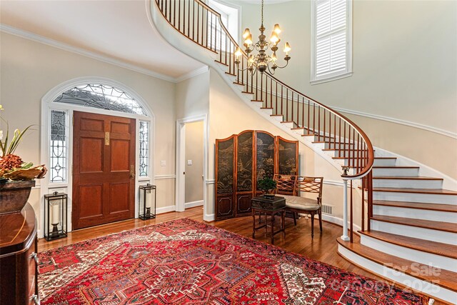 foyer entrance with stairway, a notable chandelier, crown molding, and wood finished floors