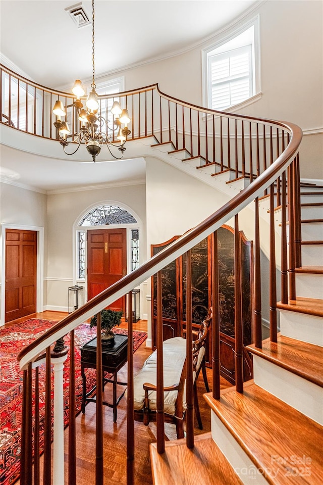 staircase with ornamental molding, visible vents, an inviting chandelier, and wood finished floors