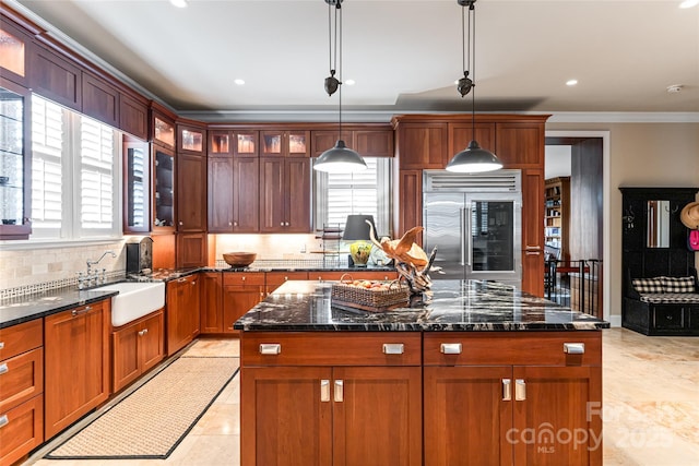 kitchen featuring dark stone countertops, a sink, built in refrigerator, ornamental molding, and backsplash