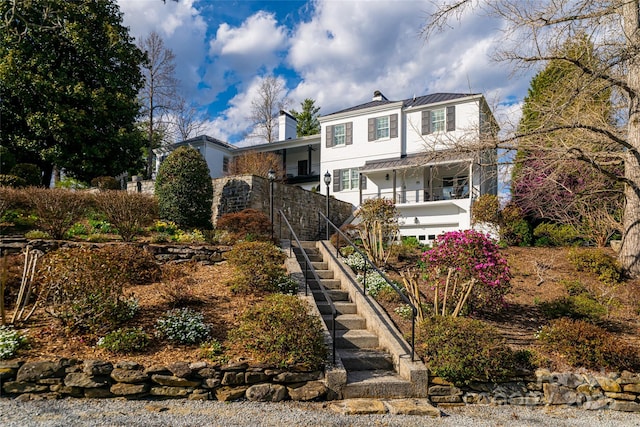 traditional home featuring stairway, a garage, a standing seam roof, metal roof, and covered porch
