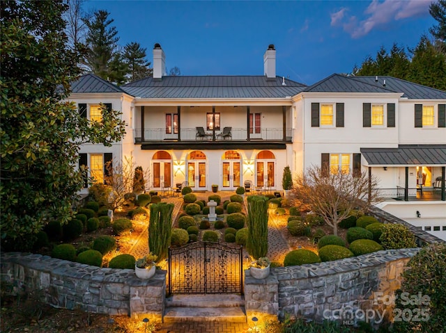 back of house with a balcony, a chimney, french doors, a standing seam roof, and metal roof