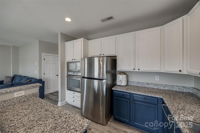 10071 Highland Creek Cir, Indian Land, SC 29707 - kitchen featuring visible vents, open floor plan, appliances with stainless steel finishes, light wood-style flooring, and blue cabinetry