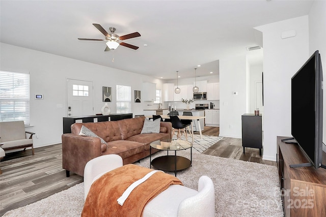 living room with baseboards, wood finished floors, visible vents, and ceiling fan