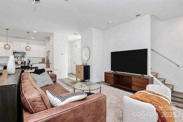 living area with stairs, light wood-style floors, visible vents, and baseboards