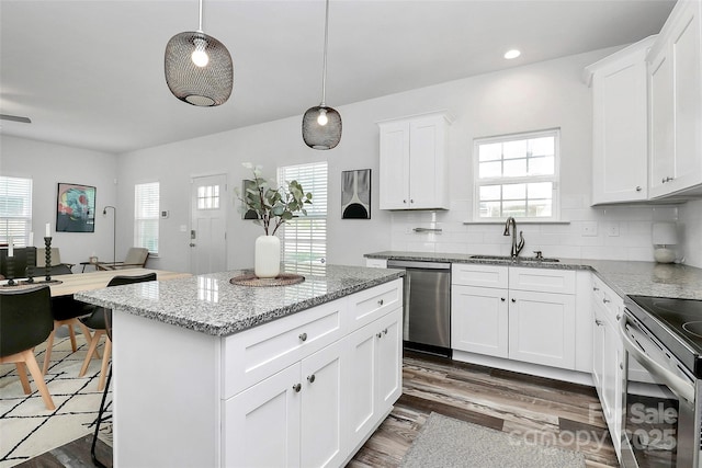 kitchen with a sink, light stone counters, wood finished floors, stainless steel appliances, and decorative backsplash