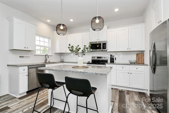 kitchen with a center island, wood finished floors, stainless steel appliances, and a sink