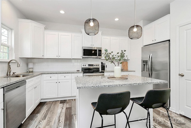 kitchen with a sink, a kitchen island, wood finished floors, appliances with stainless steel finishes, and decorative backsplash