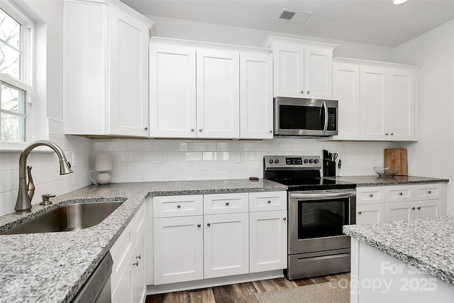 kitchen featuring visible vents, a sink, backsplash, stainless steel appliances, and white cabinets
