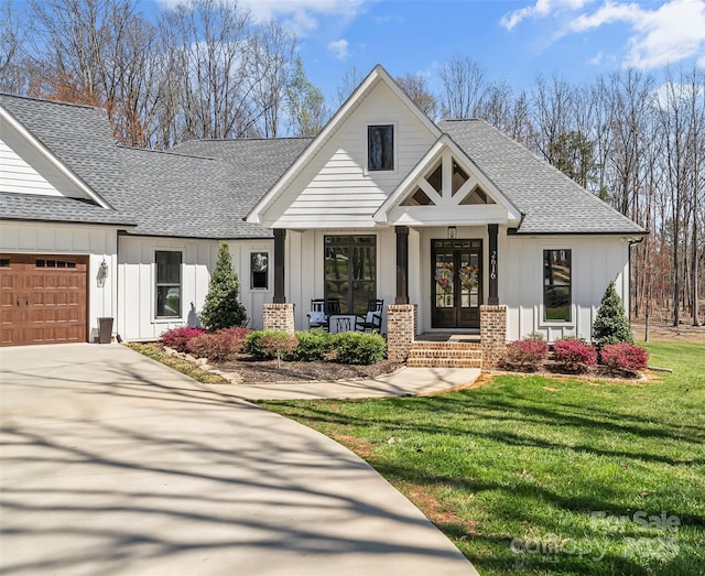 view of front of house with an attached garage, a front lawn, board and batten siding, a shingled roof, and french doors
