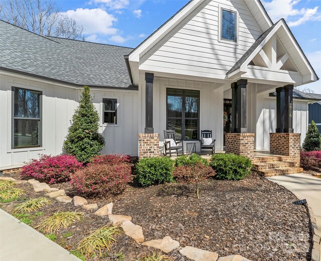 view of front of home with covered porch, board and batten siding, brick siding, and roof with shingles
