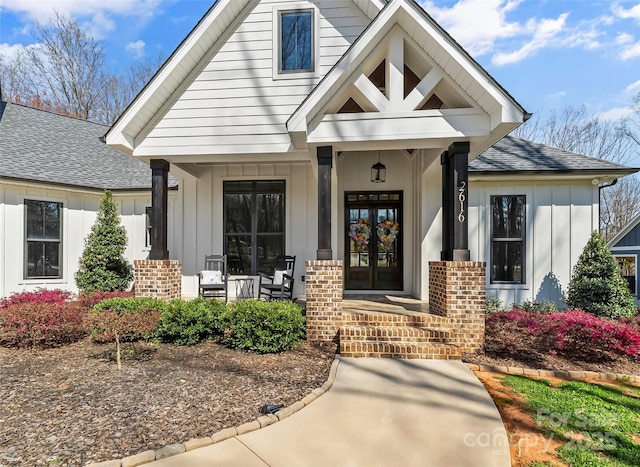 entrance to property with covered porch, french doors, board and batten siding, brick siding, and a shingled roof