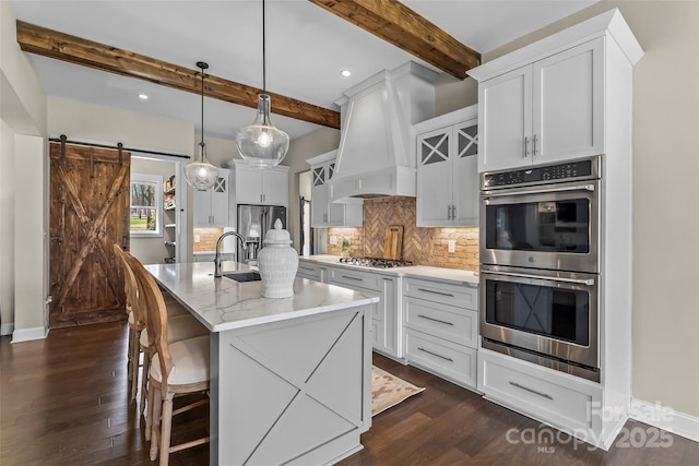 kitchen with tasteful backsplash, a sink, a barn door, appliances with stainless steel finishes, and custom exhaust hood