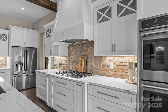 kitchen with white cabinetry, tasteful backsplash, stainless steel appliances, custom exhaust hood, and glass insert cabinets
