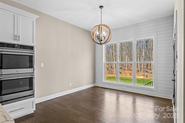unfurnished dining area with baseboards, a notable chandelier, visible vents, and dark wood-style flooring