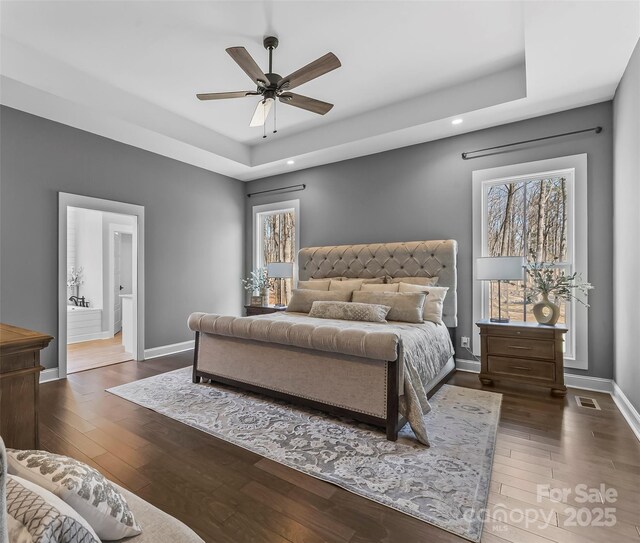 bedroom with visible vents, baseboards, dark wood finished floors, multiple windows, and a tray ceiling