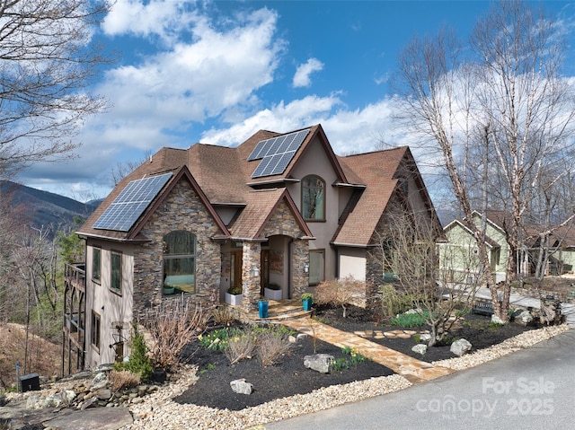 view of front of home featuring stone siding, a shingled roof, stucco siding, and solar panels