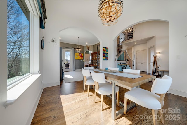 dining room with stairway, baseboards, arched walkways, a notable chandelier, and wood finished floors