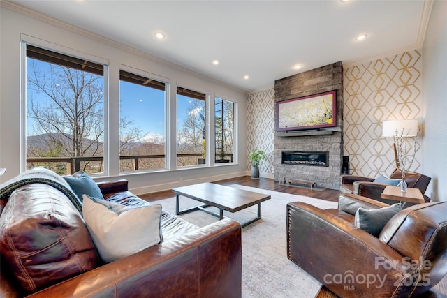 living area featuring crown molding, an accent wall, wood finished floors, a stone fireplace, and wallpapered walls